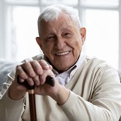 A smiling senior man sitting on a couch and holding a cane