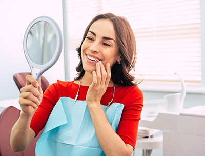 Woman in red-orange shirt in dental chair admiring smile in mirror