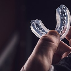 Clear mouthguard being held by fingers in front of a dark background