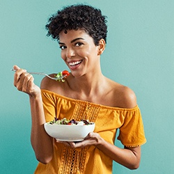 Woman in orange shirt eating a healthy salad with a pale green background