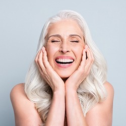 Woman with gray hair closing eyes and smiling while holding her face