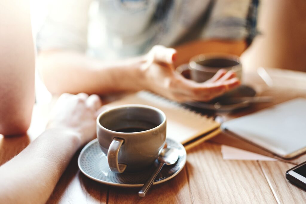 Two people leaning on table chatting with mugs of coffee